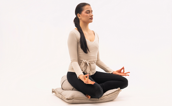 Žena sedící na meditačním polštáři Zafu a podložce Zabuton při meditaci